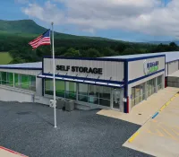 Modern self storage facility with American flag, parking, and mountainous landscape in background under blue sky.