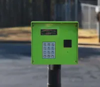 Green keypad access control panel for gated entry with numeric buttons and small display screen.