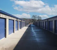 Outdoor self-storage units with blue rolling doors under a partly cloudy sky on a sunny day