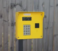 Yellow access control keypad mounted on a post in front of a wooden fence with OpenTech Alliance label.