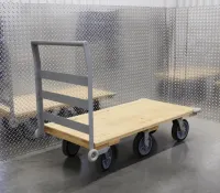 Flat wooden platform cart with metal handle and four wheels on a reflective steel floor and wall