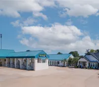 Midgard Self Storage facility with blue roofs, multiple buildings, palm trees, and clear sky with clouds.