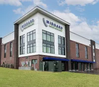 Modern Midgard Self Storage building with brick and white panel exterior under a blue sky with clouds.