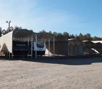 Outdoor storage units with metal roofs sheltering RVs and a covered boat under a clear blue sky.