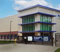 Modern self-storage facility with large windows, gated entrance, and outdoor signage under blue sky.