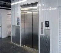 Stainless steel elevator doors in a clean storage facility hallway with white roll-up storage unit doors.