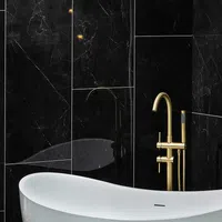 Modern white bathtub with gold faucet against sleek black marble wall tiles in a luxury bathroom