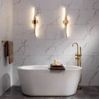 Modern bathroom with freestanding white bathtub, gold faucet, marble wall tiles, and ambient wall lights.