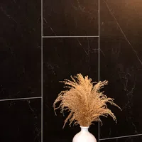 White vase with dried beige pampas grass against a black marble tile wall with white grout lines.