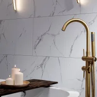 Modern bathroom with marble wall tiles, gold faucet, bathtub, and three lit white candles on wooden tray.