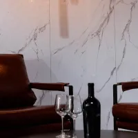 Two leather chairs with a wine bottle and two empty wine glasses on a table against a marble wall.