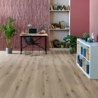 Modern home office with textured mauve wall, wooden desk, black chair, plants, and light wood flooring.