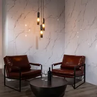 Cozy seating area with two brown leather chairs, round black table, wine bottle, glasses, and hanging pendant lights.