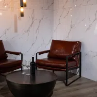 Modern lounge area with brown leather armchairs, black round coffee table, wine bottle, and glasses on wood floor.