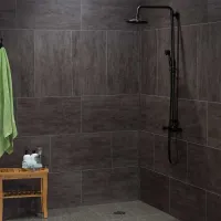 Modern shower area with dark gray tiles, black shower fixtures, wooden stool, and green towel hanging