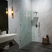 Modern bathroom with marble tile walls, walk-in glass shower, wooden stool, and hanging pendant lights.