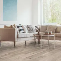 Modern beige sectional sofa with patterned cushions and nested coffee tables in bright living room with wood flooring.
