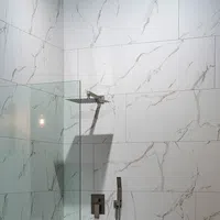 Modern walk-in shower with large rain showerhead and white marble wall tiles with gray veining.