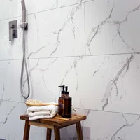 Modern shower area with marble wall tiles, wooden stool holding towels, brush, and amber soap dispensers.