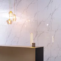 Modern interior with a sleek beige countertop and glowing pendant lights against marble wall tiles.