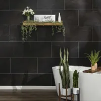 Modern bathroom with dark tile wall, freestanding white tub, wooden floor, floating shelf with plants and decor.