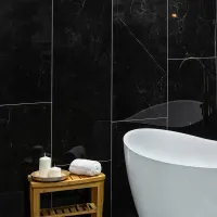 Modern bathroom with white freestanding tub, rolled towel, candles on wooden stool, and black marble walls.
