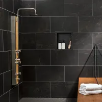 Modern black tiled shower with stainless steel shower panel, built-in shelf with bottles, and wooden bench with towels