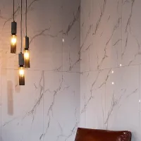 Modern hanging pendant lights illuminated against a white marble wall with gray veining beside a brown leather chair.