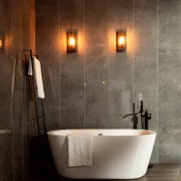 Modern bathroom with white freestanding bathtub, towel rack, warm wall sconces, and gray marble walls.