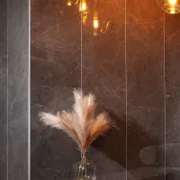 Decorative dried pampas grass in clear vase against dark marble wall with warm hanging lights.