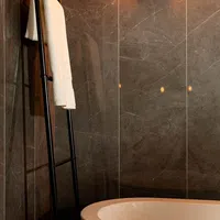 Modern bathroom with dark marble walls, freestanding white bathtub, and black towel ladder with white towel.