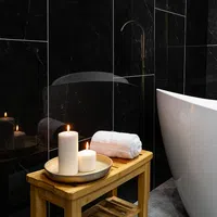 Wooden bench with lit candles and a rolled towel next to a white bathtub in a black marble bathroom.