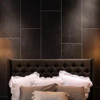 Dark tufted headboard with white ruffled pillows and textured beige throw pillow against black marble wall.