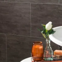 Bathroom corner with dark wall tiles, a white sink, amber glass candle holder, and a white rose in a clear vase.