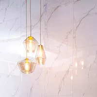 Three modern glass pendant lights glowing against white marble wall with grey veins in minimalist interior.