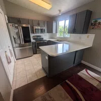 Modern kitchen with gray cabinets, stainless steel appliances, white countertops, tile and dark wood flooring.