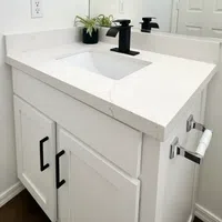 Modern white bathroom vanity with black faucet, marble countertop, and small potted plant near mirror.