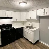 Modern kitchen with white cabinets, black appliances, wood flooring, and a ceiling light fixture.