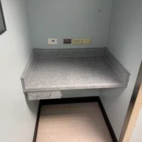 Small gray countertop workspace with wall outlets and a red switch on white walls in a confined room.