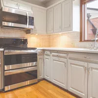 Bright kitchen with white cabinets, stainless steel oven and microwave, beige tiled backsplash, and wooden floor.