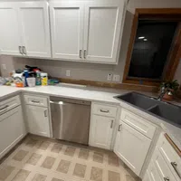 Modern kitchen with white cabinets, stainless steel dishwasher, black sink, and beige patterned tile floor.