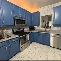 Modern kitchen with blue cabinets, stainless steel appliances, gray countertops, and white marble tile flooring.