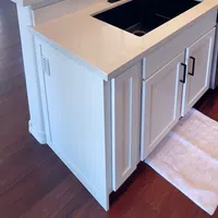 Modern kitchen island with white cabinetry, black sink, black faucet, beige countertop, and hardwood flooring.