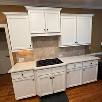 Modern kitchen with white cabinets, beige tiled backsplash, gas stovetop, and hardwood flooring with black floor mat.