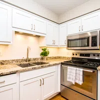 Modern kitchen with white cabinetry, granite countertops, double sink, stainless steel stove and microwave.