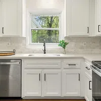 Modern white kitchen with stainless steel appliances, marble backsplash, and window overlooking greenery.