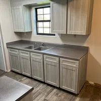 Modern kitchen with light wood cabinets, gray countertops, stainless steel sink, and wood grain flooring.