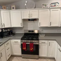Modern kitchen with white cabinets, gray countertops, stainless steel gas stove, and microwave oven with red towels.