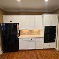 Modern kitchen section with white cabinets, black Whirlpool refrigerator and built-in double oven on hardwood floor.