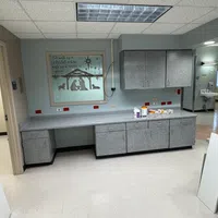Empty room with gray cabinets, countertop, nativity scene wall art, fluorescent ceiling lights, and hospital-style interior.